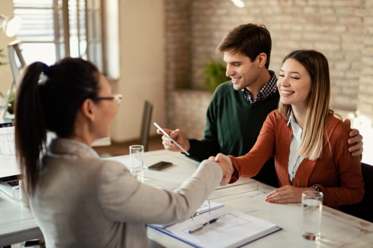 young happy woman shaking hands with real estate agent while her husband is using touchpad office